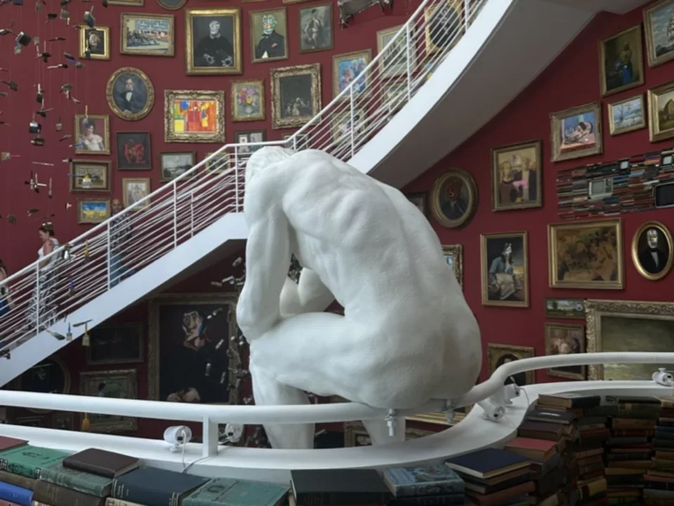 Statue sitting on railing surrounded by books in a pondering stance.  