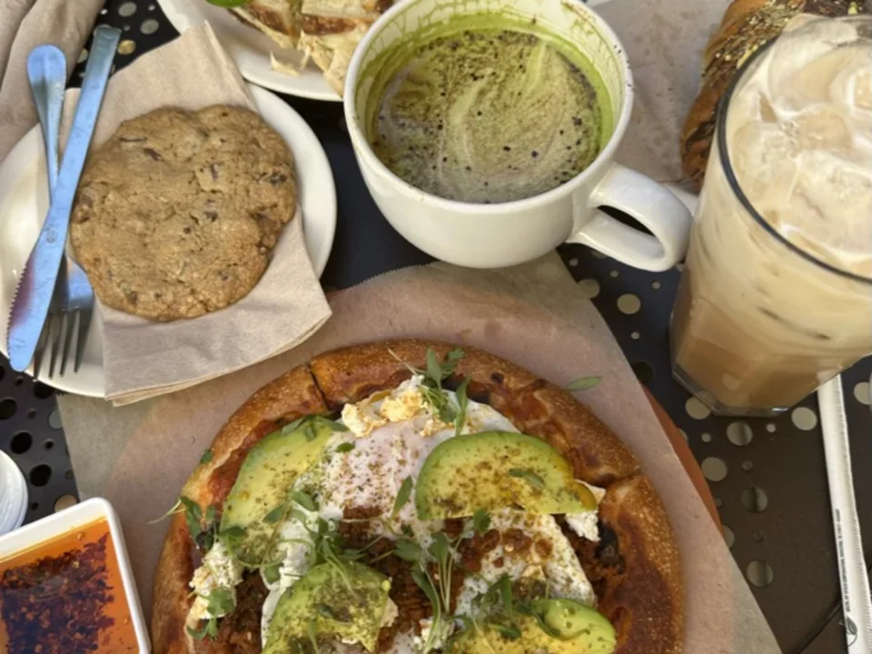 Eggs with avocado and cilantro. Cookie on a napkin next to a fork and butter knife with matcha latte on the side. 