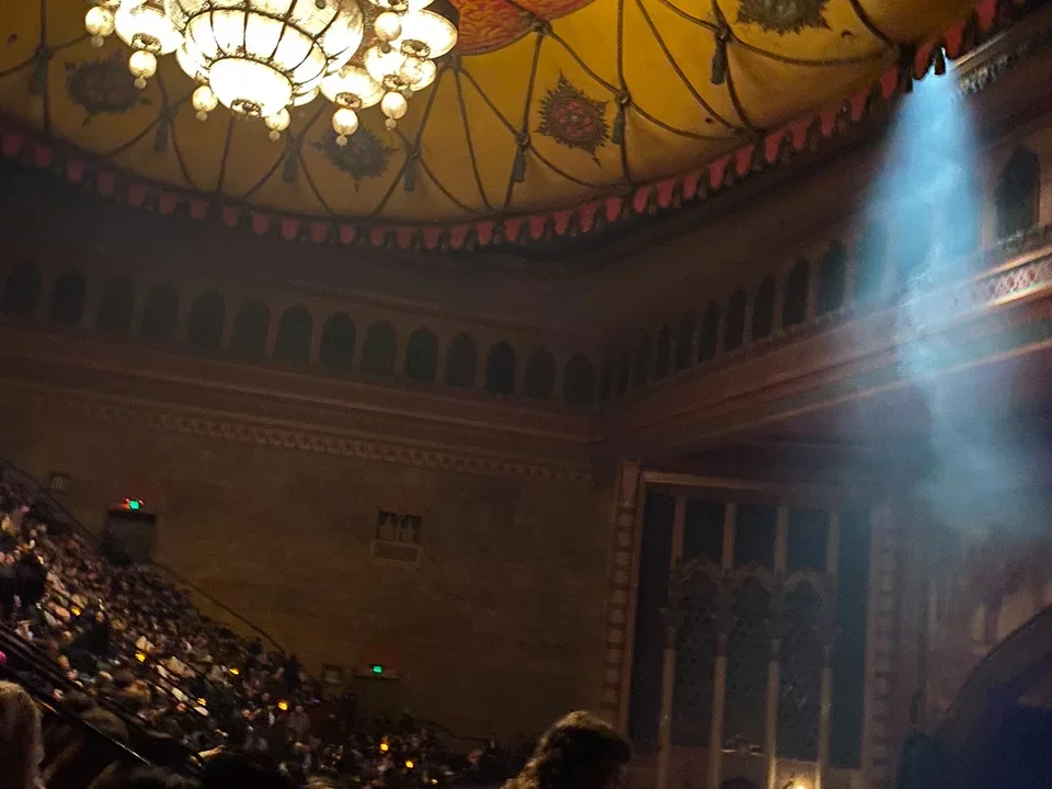 Theatre crowd under a bright chandelier. 