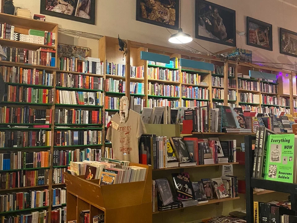 Books on shelves in a bookstore with framed posters above said bookshelves. 