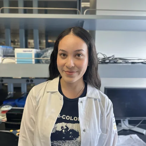 Gizelle Ramirez in front of a lab bench bay while wearing a lab coat.