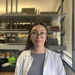 Kimberly Jorge in front of a lab bench bay while wearing a white lab coat 